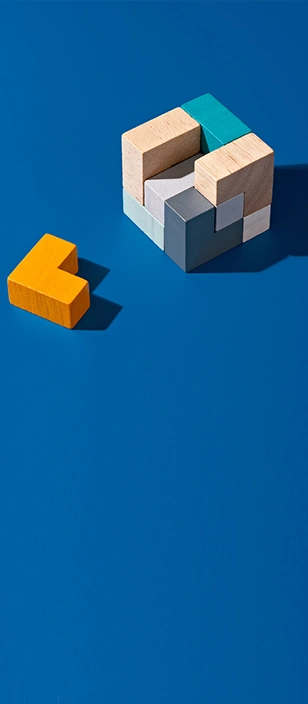 Blocchi di legno colorati su sfondo blu che formano un cubo quasi completo con un pezzo giallo a forma di L posizionato accanto.