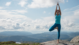 Donna in posizione yoga sulla vetta di una montagana con panorama di sfondo